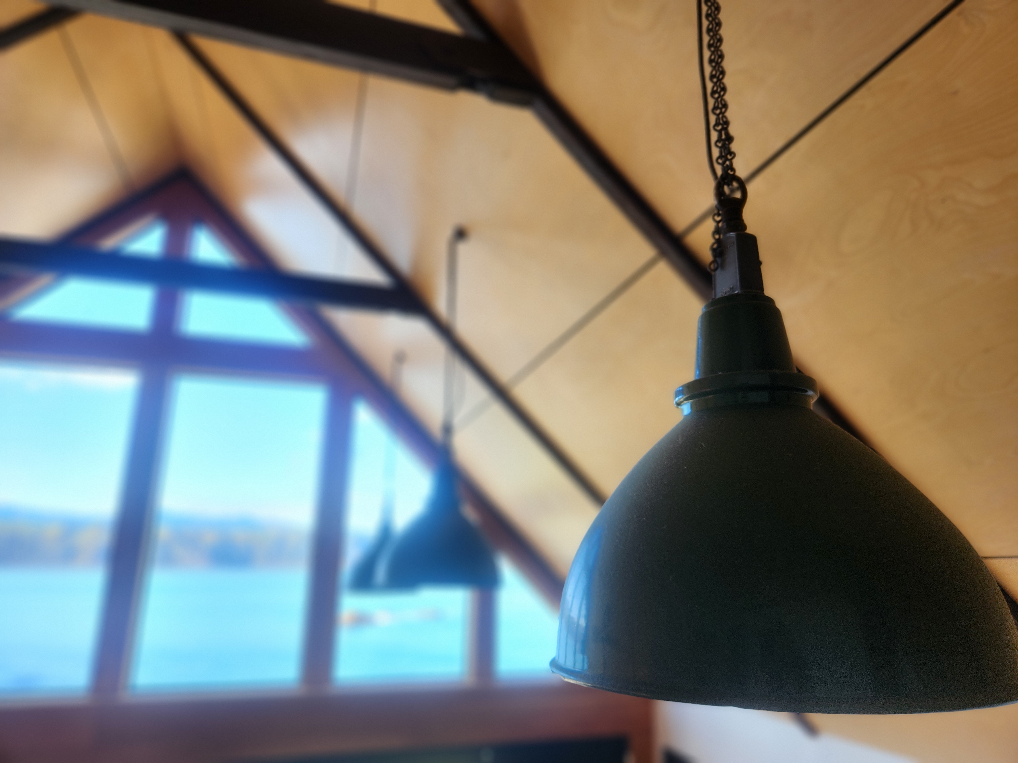 A line-up of three green industrial shades by Thorlux. Against a backdrop of a Birch lined A frame ceiling with sea, mountains and blue sky in the background.