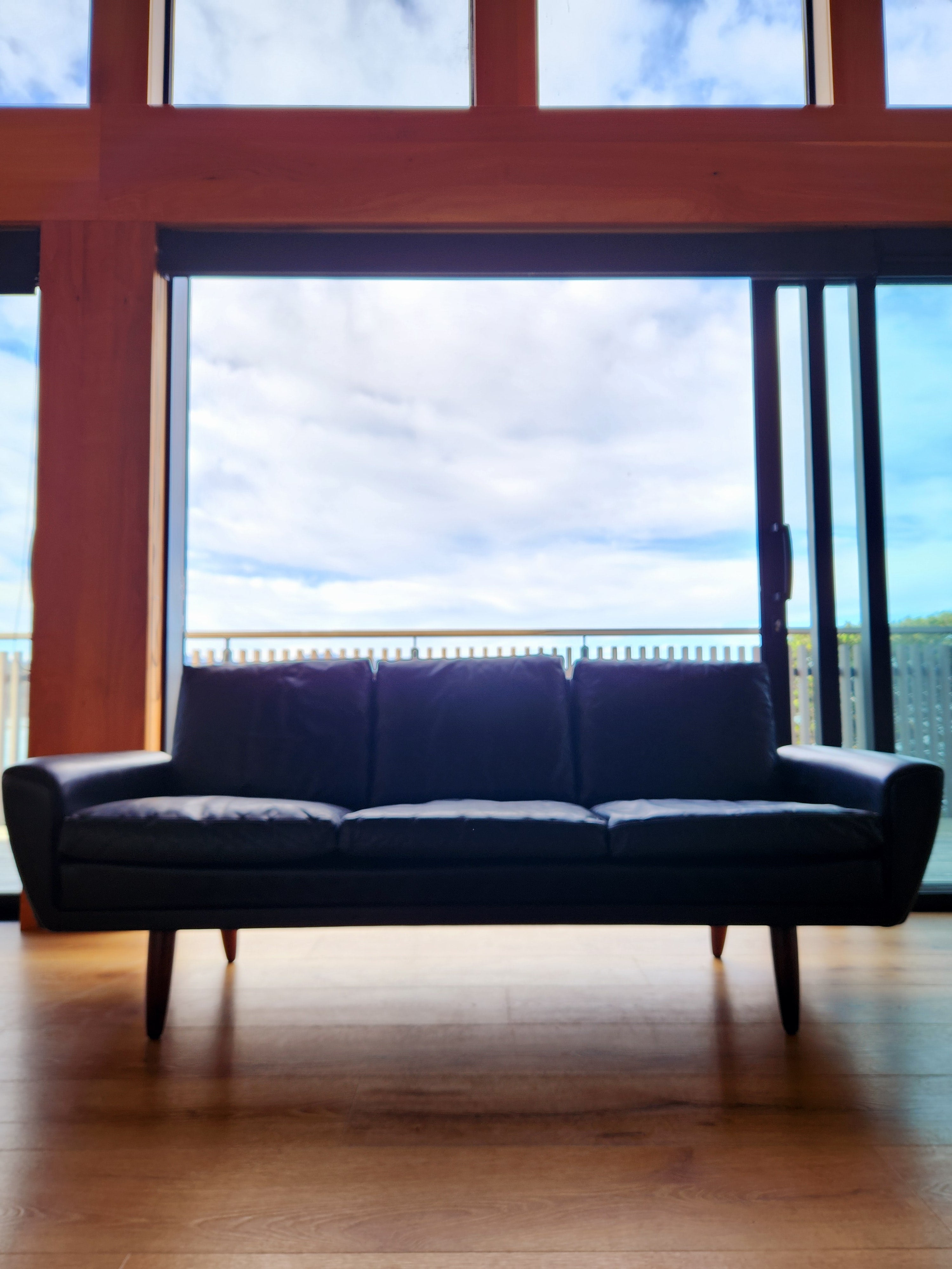 Danish mid century sofa. Backlit Portrait of sofa from in front of architectural windows. 