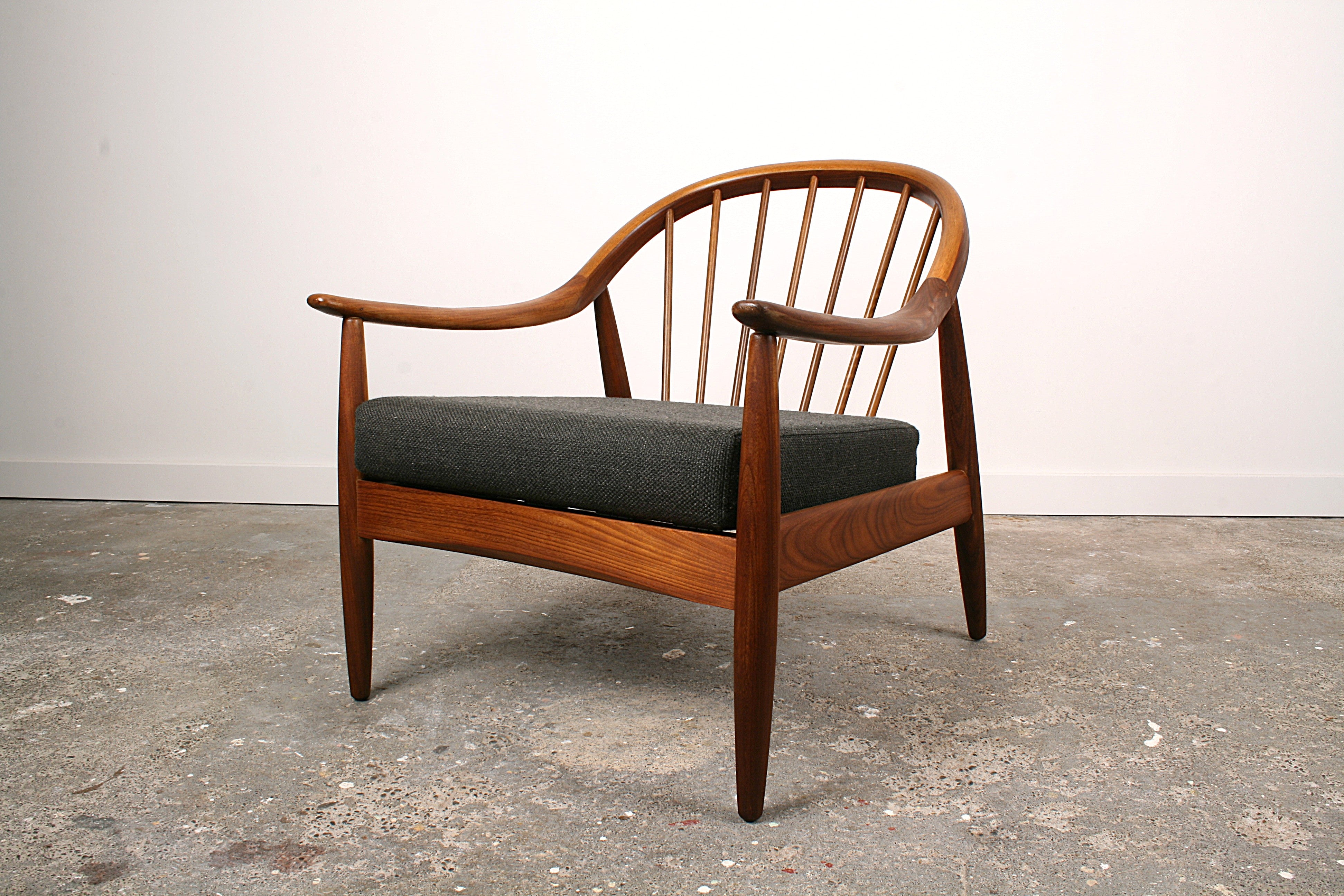 1960's Mid Century Teak armchair by Greaves and Thomas with a curved spindle back and charcoal black/grey upholstery. Spindles revealed.