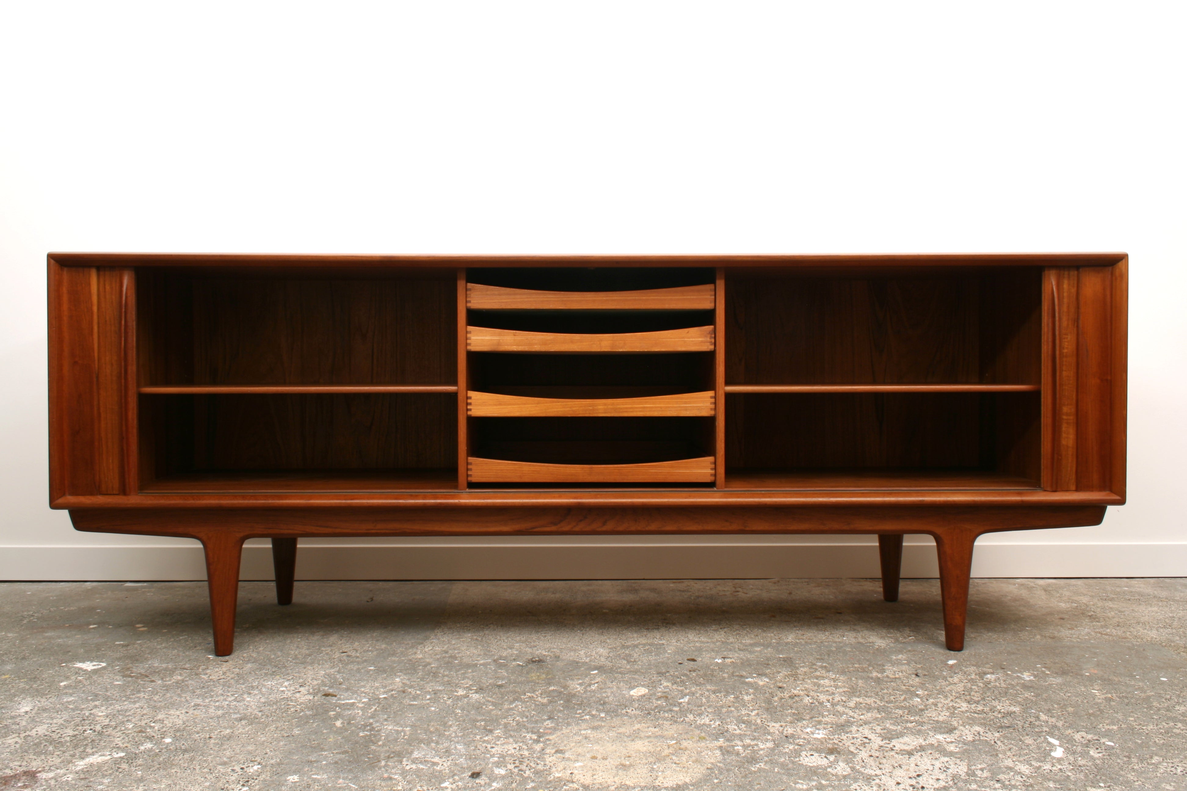 A Model 156 Danish Teak tambour sideboard by Bernhard Pedersen & Son. Shown from the front with doors open revealing a central bank of four drawers. Flanked by cupboard space with an adjustable shelf.