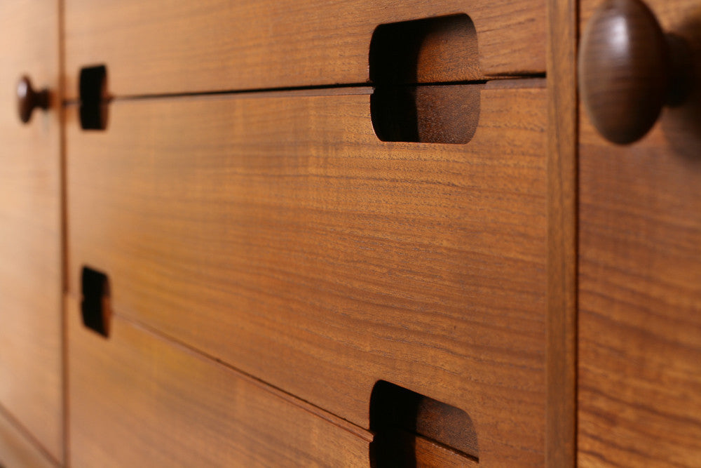 Close up of a Teak mid century sideboard detailng straight woodgrain, round door handles and recessed, lozenge shaped, drawer pulls.