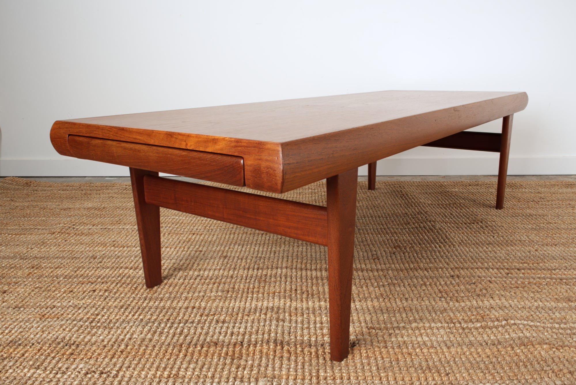 Johannes Andersen designed coffee table in Teak. From end profile with inset drawer closed.