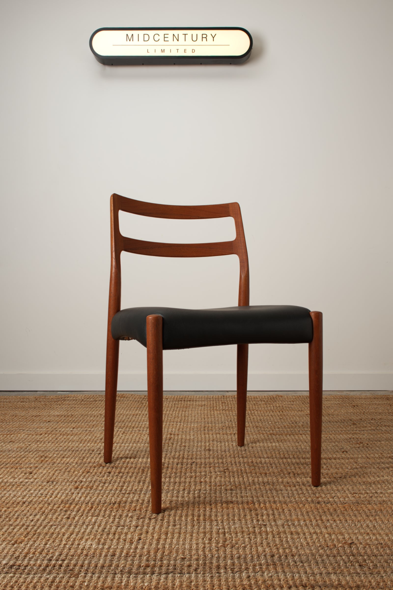 A single Johannes Andersen Danish chair. With a Midcentury Limited lightbox in the background.