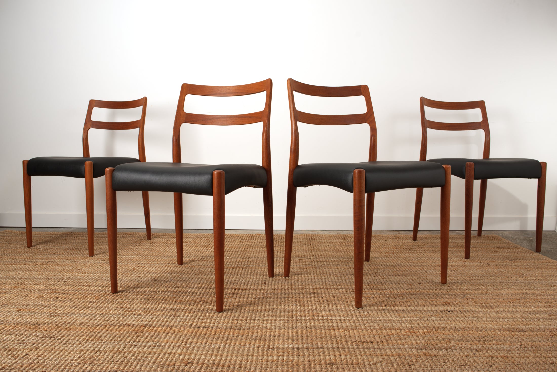 Four Johannes Andersen Danish Teak chairs highlighting their elegant structure.