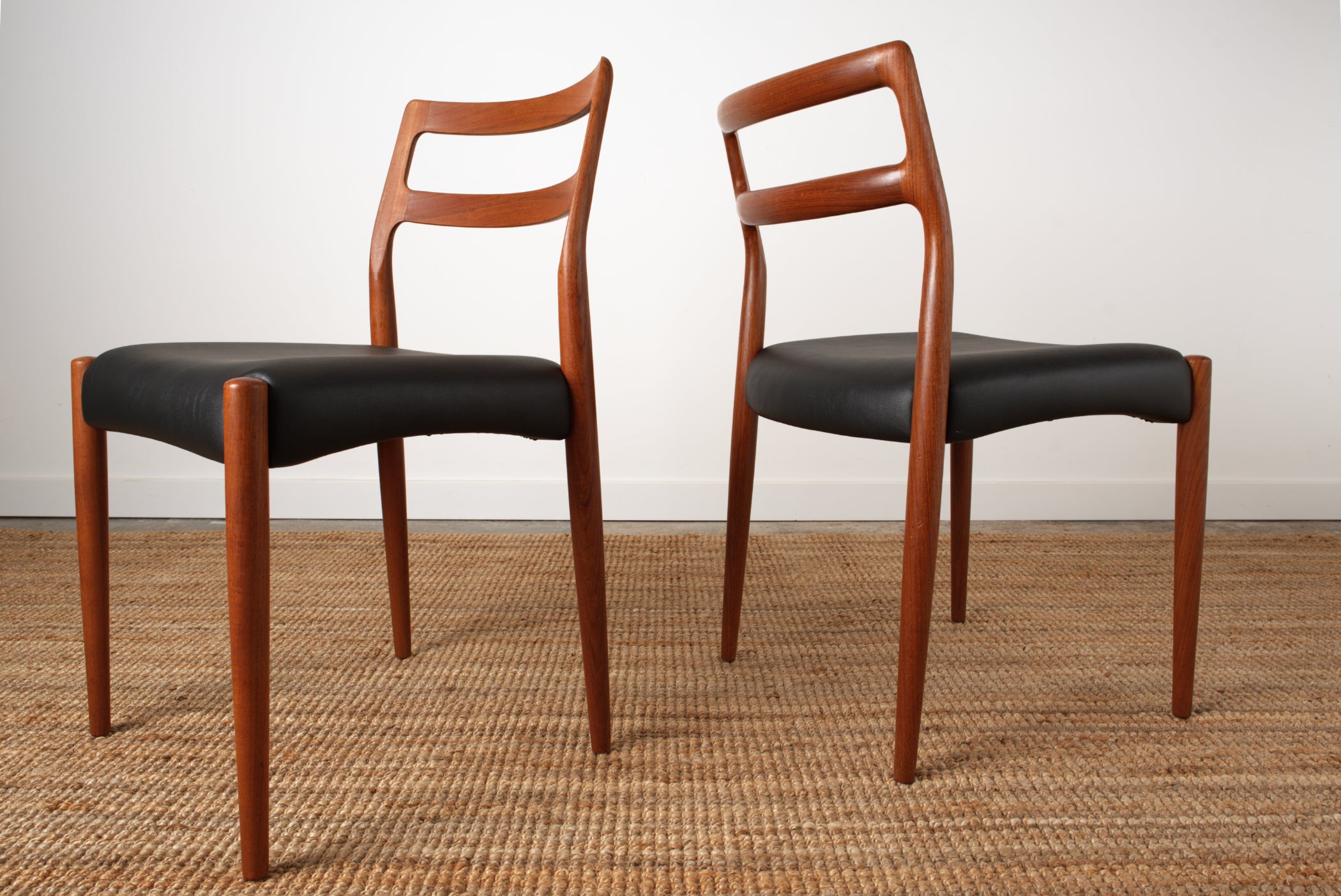 A pair if Johannes Andersen Danish chairs showing off the the sculpted curves of the back rest rails. side view.