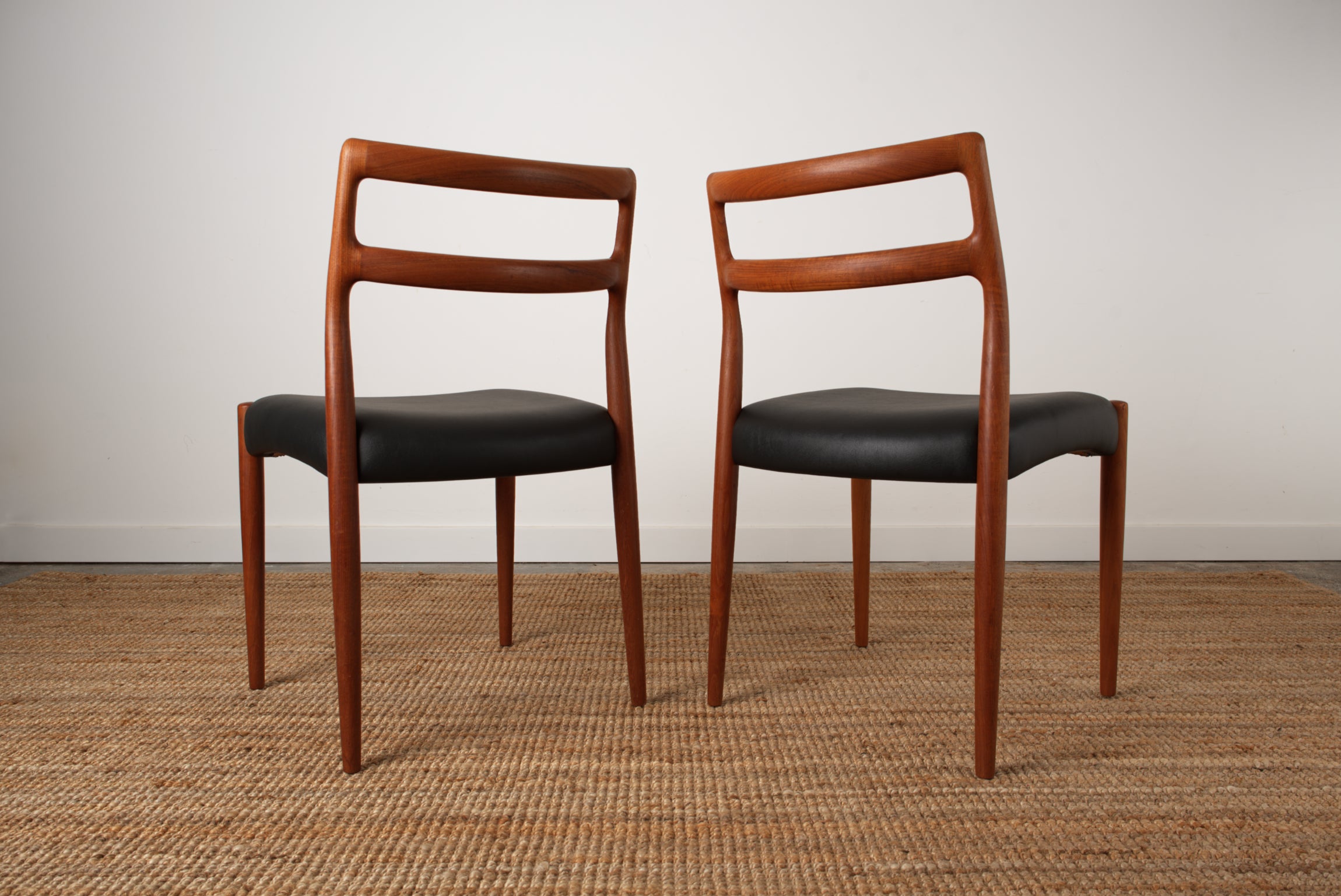 A pair if Johannes Andersen Danish chairs showing off the the sculpted curves of the back rest rails from the rear.